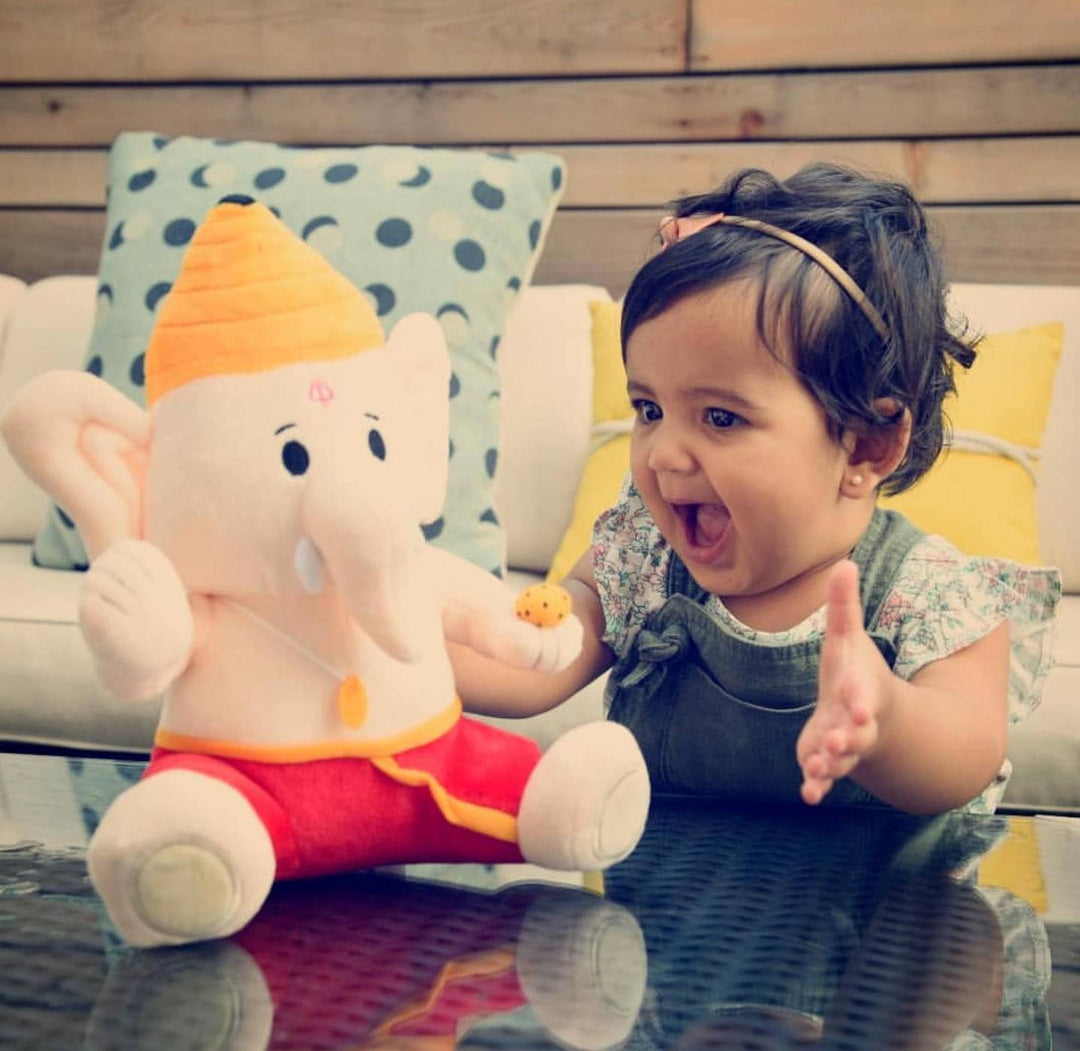 child laughing next to baby ganesh plush toy