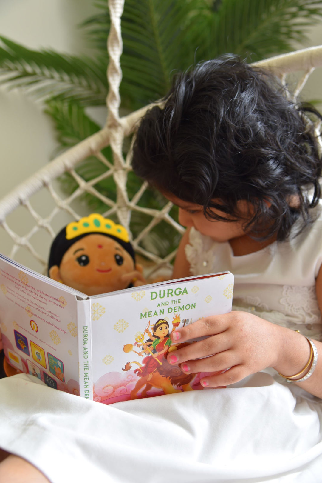 child reading "Durga and the mean demon" to a Durga Devi plush toy