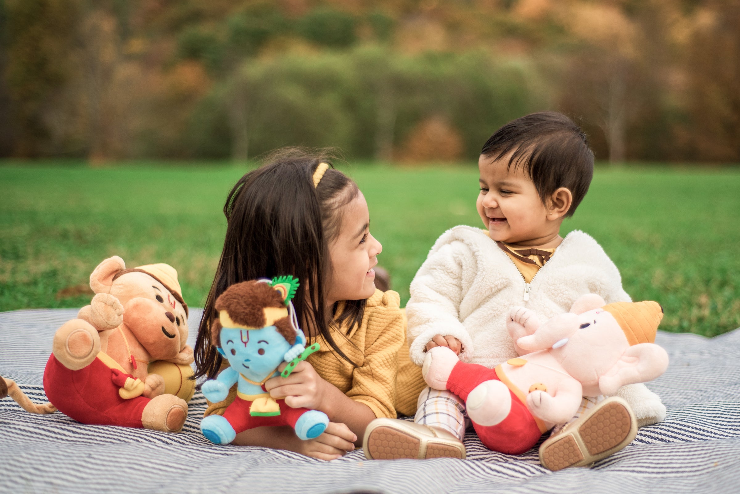 girl and boy smiling at each other outside with baby ganesh & baby krishna & baby hanuman plush toys
