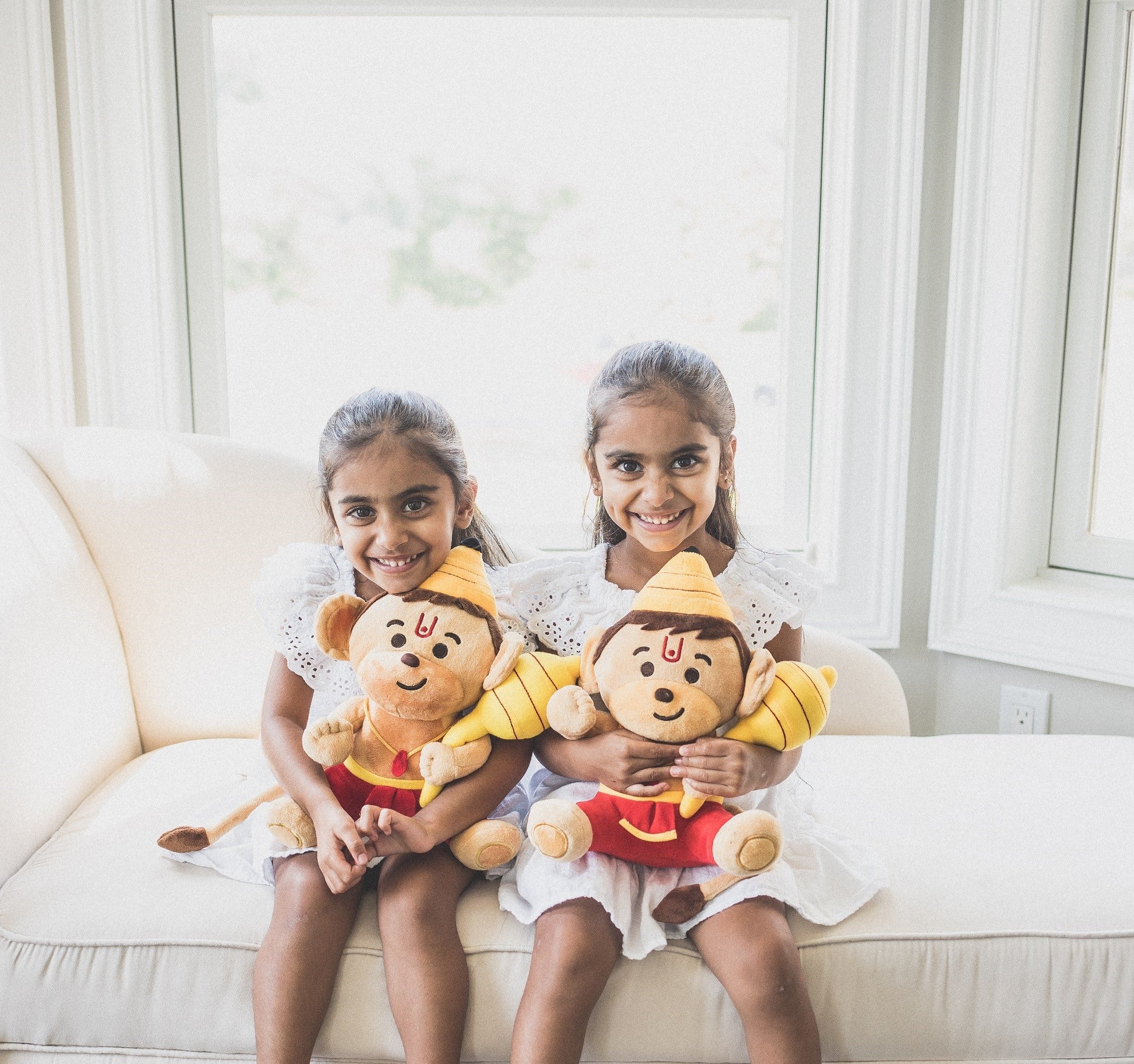 two smiling children holding baby hanuman plush toys